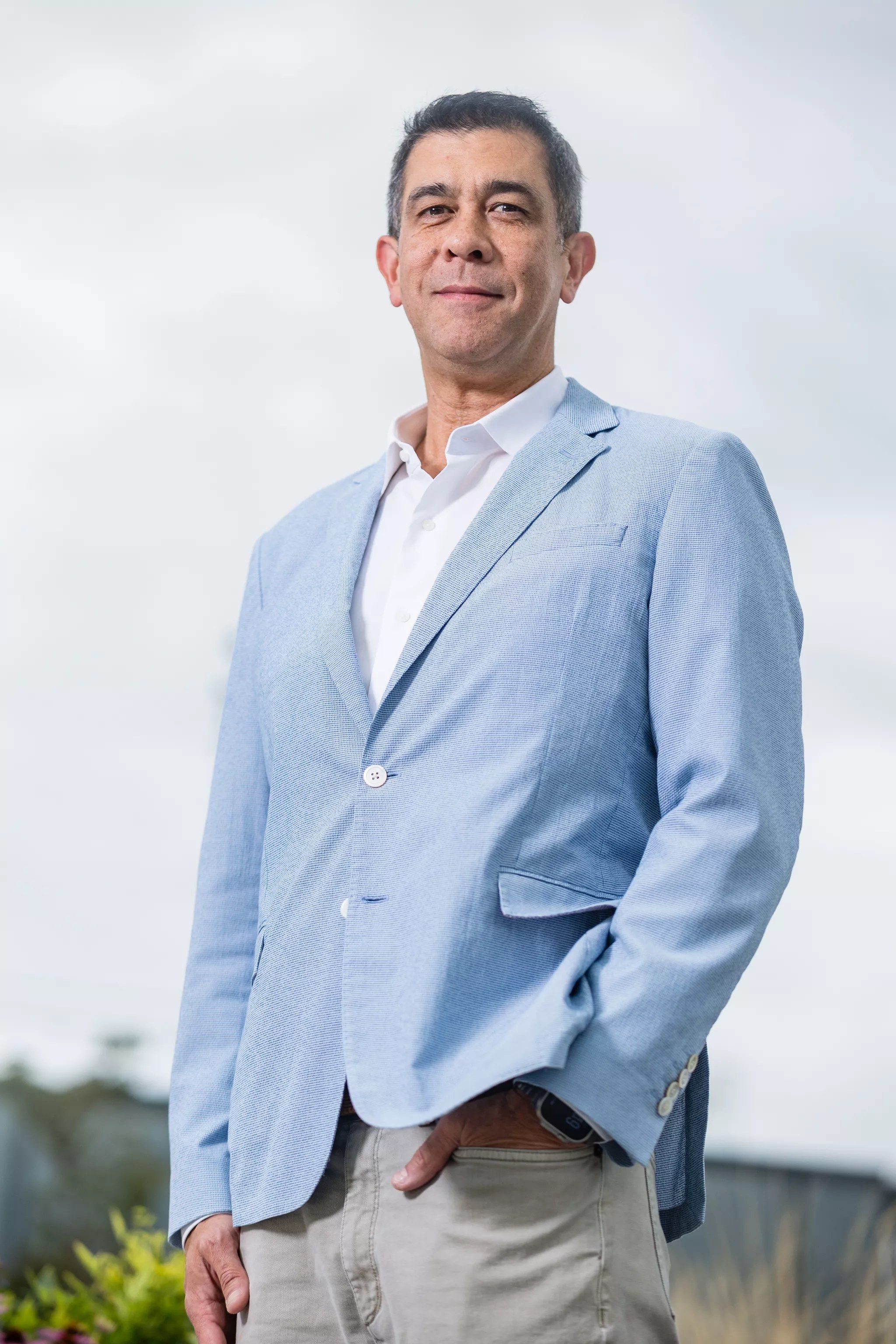 Darin Grant in a light blue blazer, standing outdoors against a pale sky
